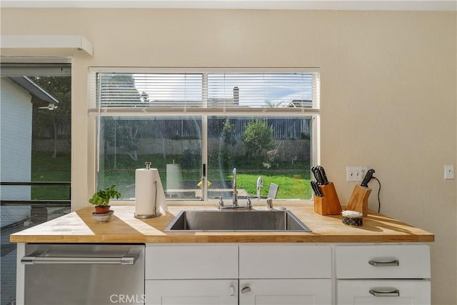 kitchen featuring dishwasher, sink, white cabinets, and butcher block countertops