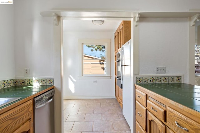 kitchen with tile counters, light tile patterned floors, backsplash, and appliances with stainless steel finishes