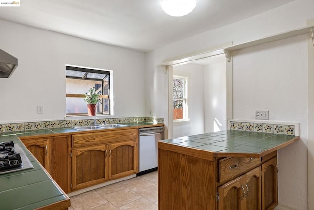 kitchen featuring light tile patterned floors, tile countertops, kitchen peninsula, stainless steel dishwasher, and sink