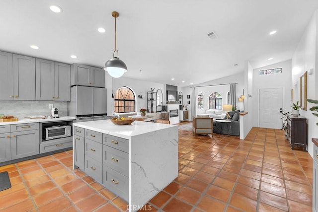 kitchen featuring vaulted ceiling, gray cabinets, hanging light fixtures, and light stone countertops