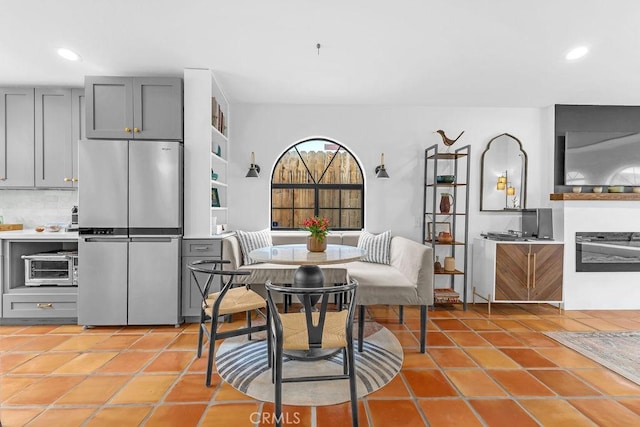 kitchen featuring light tile patterned flooring, gray cabinetry, tasteful backsplash, and stainless steel refrigerator