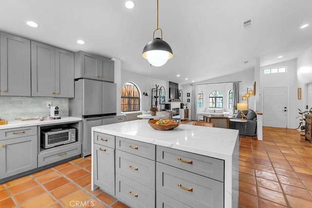 kitchen with appliances with stainless steel finishes, gray cabinetry, decorative backsplash, lofted ceiling, and hanging light fixtures