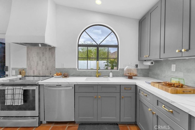 kitchen with custom exhaust hood, stainless steel appliances, gray cabinetry, light stone counters, and sink