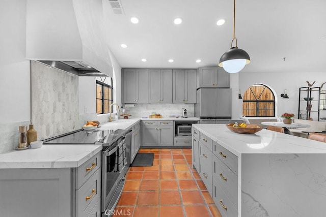 kitchen featuring appliances with stainless steel finishes, wall chimney range hood, light stone counters, and gray cabinets