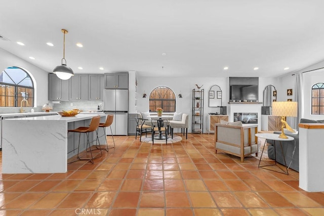 kitchen featuring a kitchen bar, gray cabinets, tasteful backsplash, hanging light fixtures, and refrigerator