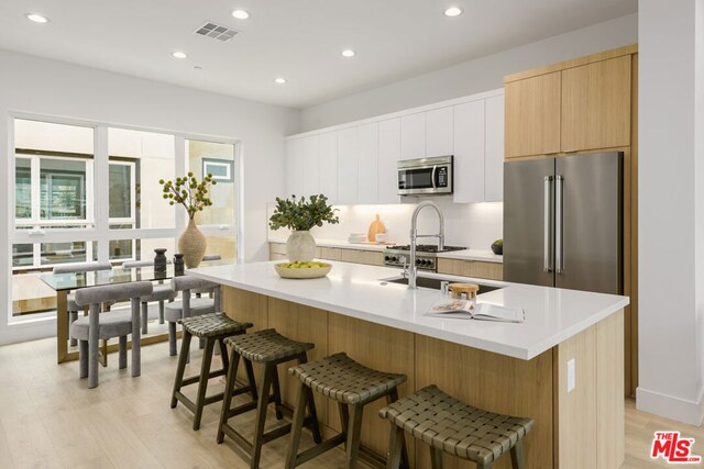 kitchen featuring a center island with sink, white cabinetry, light wood-type flooring, appliances with stainless steel finishes, and a kitchen breakfast bar