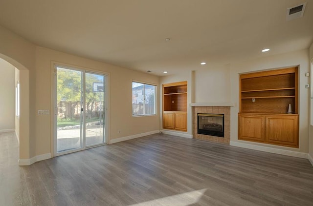 unfurnished living room featuring built in shelves, a fireplace, and hardwood / wood-style floors