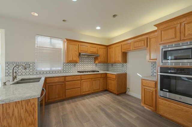 kitchen with backsplash, hardwood / wood-style floors, sink, appliances with stainless steel finishes, and light stone counters