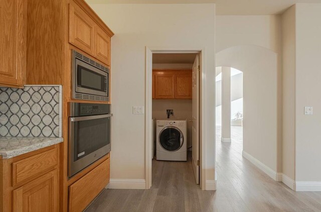 kitchen with light stone countertops, washer / dryer, stainless steel appliances, backsplash, and light hardwood / wood-style flooring