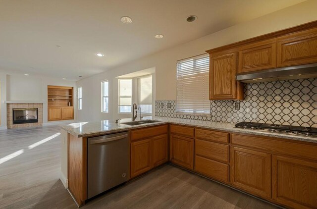 kitchen with light stone countertops, stainless steel appliances, a fireplace, sink, and hardwood / wood-style flooring