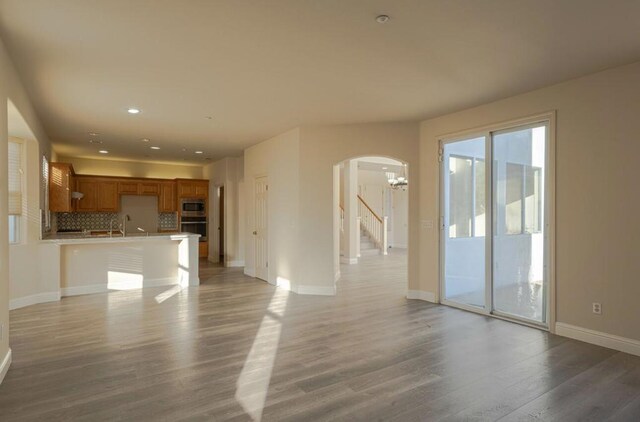 unfurnished living room with sink, an inviting chandelier, and light wood-type flooring