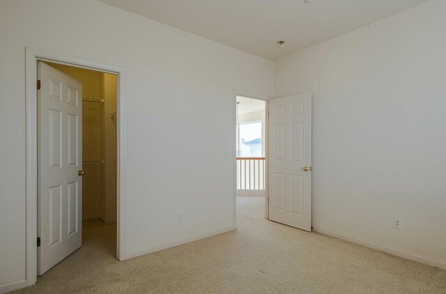 unfurnished bedroom featuring a spacious closet, a closet, and light carpet