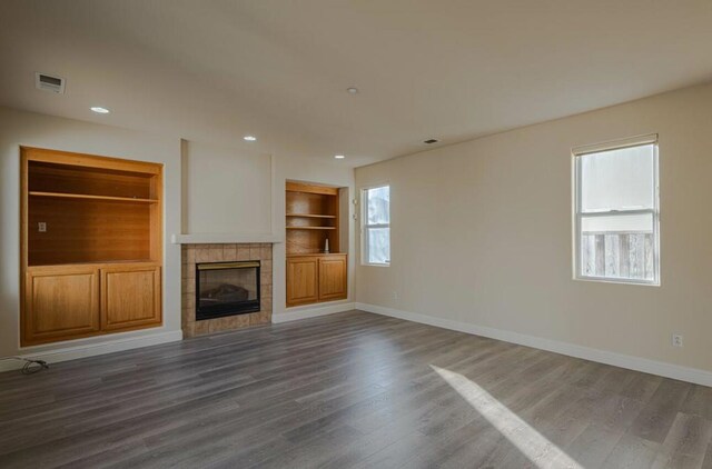 unfurnished living room with dark hardwood / wood-style flooring, a tile fireplace, and built in shelves