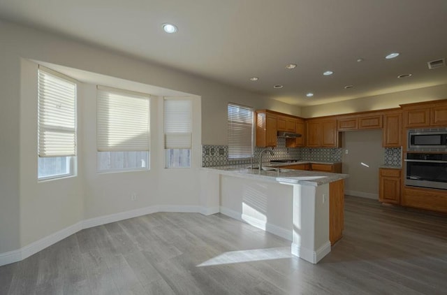 kitchen with exhaust hood, light hardwood / wood-style floors, kitchen peninsula, stainless steel appliances, and decorative backsplash