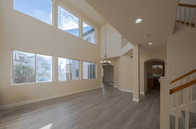 unfurnished living room featuring a high ceiling, an inviting chandelier, and wood-type flooring