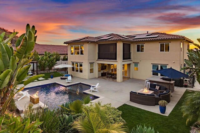 back house at dusk with an outdoor living space with a fire pit, a patio area, and solar panels