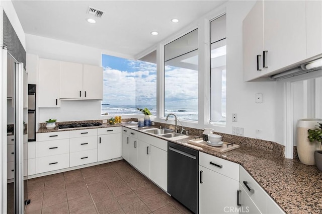 kitchen featuring appliances with stainless steel finishes, white cabinetry, dark stone counters, and sink