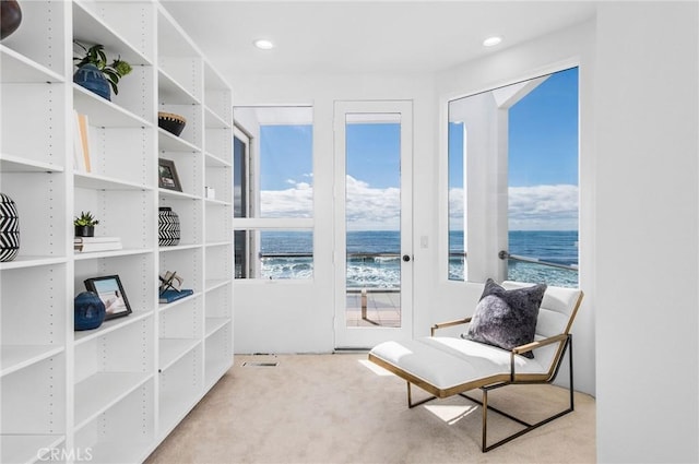 sitting room with light colored carpet, a water view, and a beach view