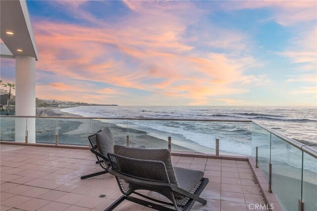 balcony at dusk featuring a water view and a view of the beach