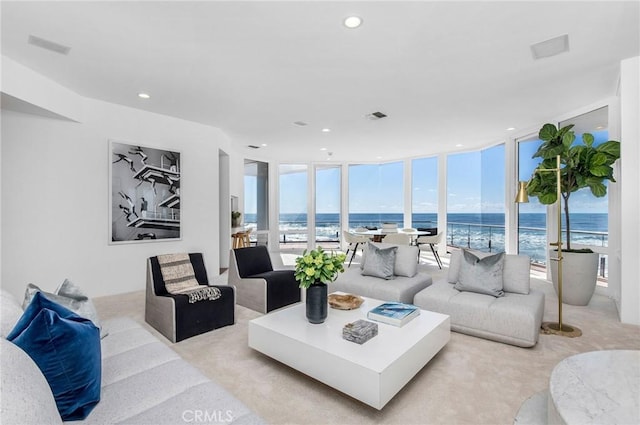 living room with light carpet, a water view, a beach view, and expansive windows