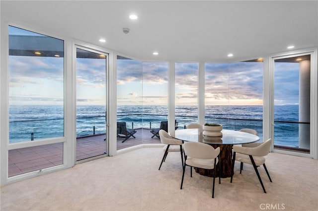 dining area featuring a view of the beach, a wall of windows, a water view, and light colored carpet