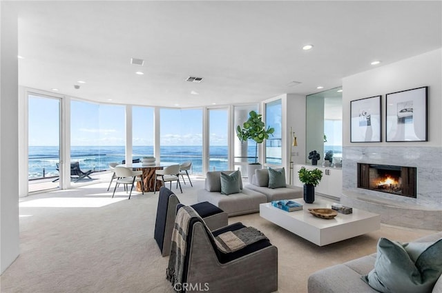 living room with light colored carpet, expansive windows, a water view, and a fireplace