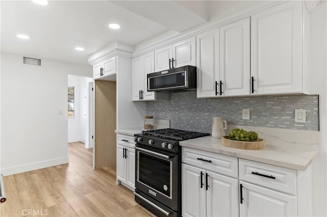 kitchen featuring high end stove, tasteful backsplash, light wood-type flooring, light stone countertops, and white cabinets