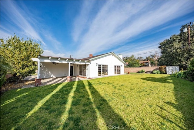 rear view of property with ceiling fan, a patio, and a yard