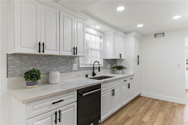 kitchen with tasteful backsplash, stainless steel dishwasher, sink, white cabinetry, and light wood-type flooring