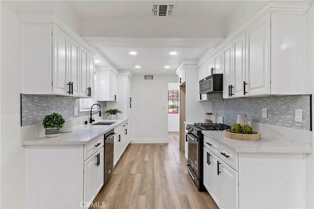 kitchen featuring light stone countertops, white cabinets, appliances with stainless steel finishes, sink, and backsplash