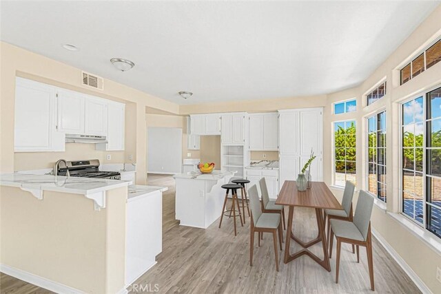 kitchen featuring white cabinetry, light hardwood / wood-style flooring, stainless steel range oven, and a breakfast bar area