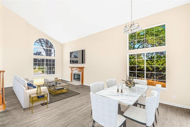 dining room featuring high vaulted ceiling, a wealth of natural light, wood-type flooring, and a notable chandelier