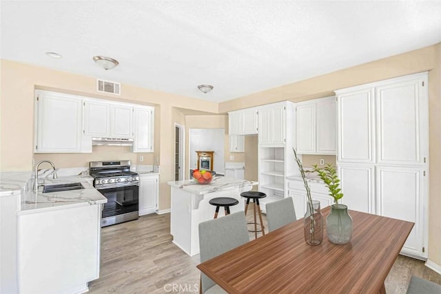 kitchen with light wood-type flooring, stainless steel gas stove, sink, and white cabinetry