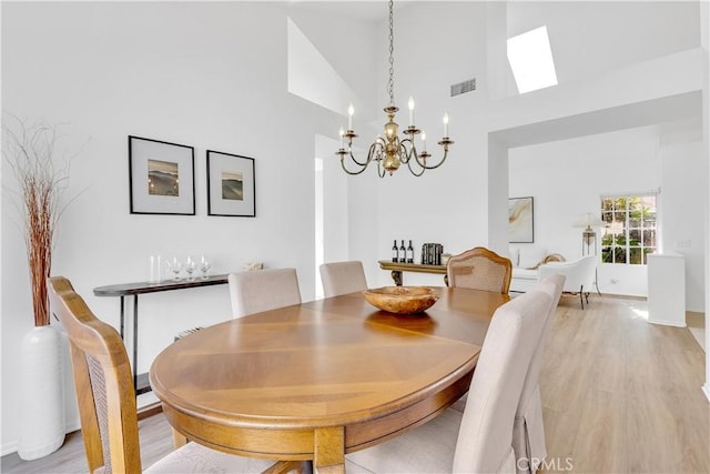 dining room featuring high vaulted ceiling, a skylight, a notable chandelier, and light hardwood / wood-style floors