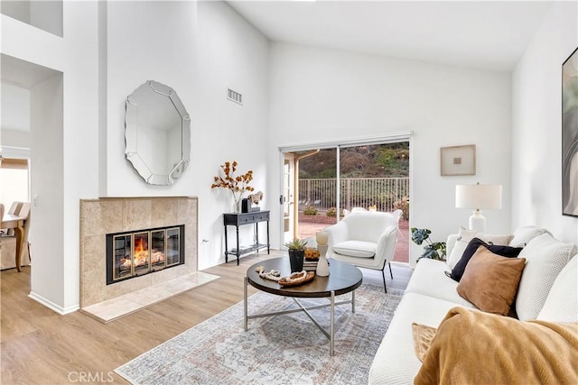 living room featuring light wood-type flooring, a towering ceiling, and a tiled fireplace