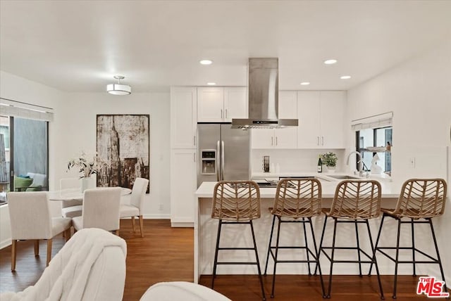 kitchen with exhaust hood, sink, white cabinetry, a kitchen breakfast bar, and stainless steel fridge