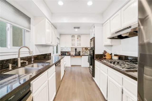 kitchen with white cabinetry, light hardwood / wood-style floors, stainless steel appliances, dark stone countertops, and sink