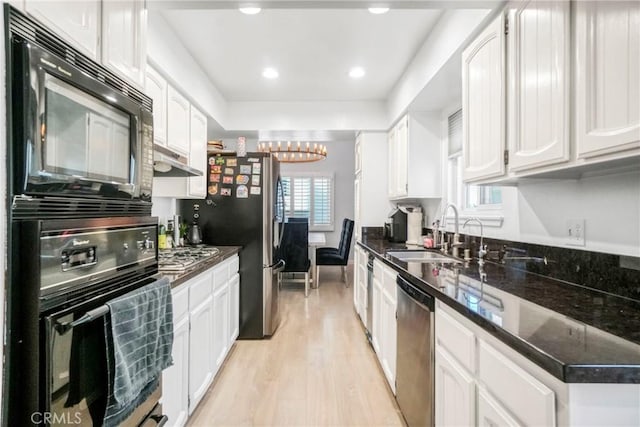 kitchen featuring dark stone countertops, black appliances, sink, an inviting chandelier, and white cabinetry