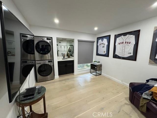 laundry room with stacked washer / dryer, light hardwood / wood-style flooring, and sink