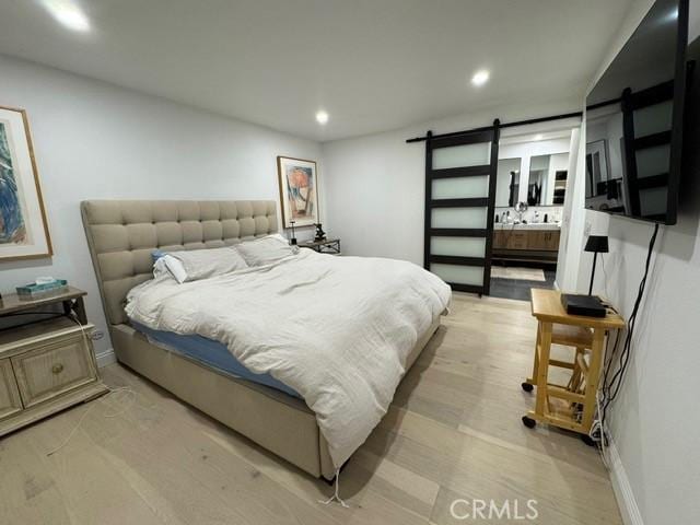 bedroom featuring light hardwood / wood-style floors, connected bathroom, and a barn door