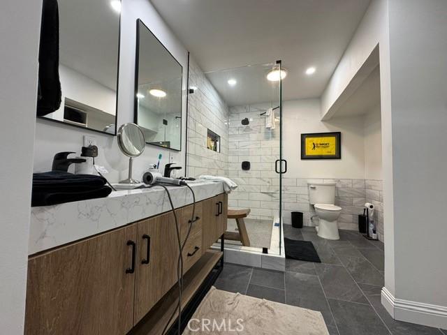 bathroom featuring toilet, vanity, tile walls, tile patterned floors, and a shower with door