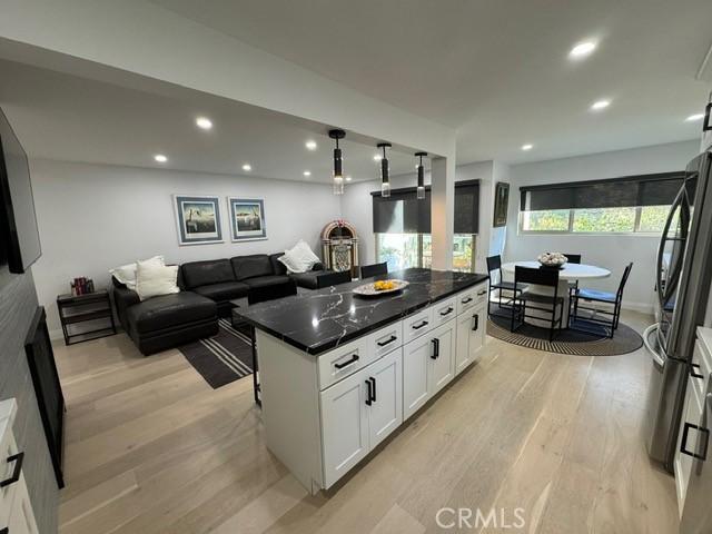 kitchen with white cabinetry, stainless steel fridge, dark stone countertops, a kitchen island, and light hardwood / wood-style flooring