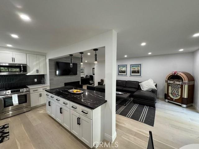 kitchen with tasteful backsplash, light hardwood / wood-style floors, hanging light fixtures, stainless steel appliances, and white cabinets