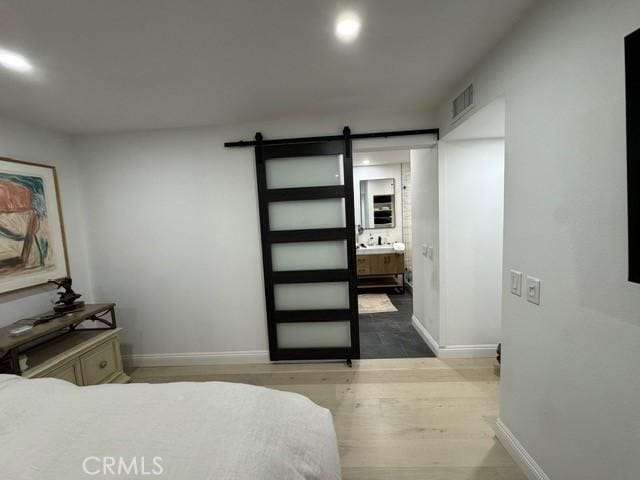 bedroom featuring a barn door, connected bathroom, and hardwood / wood-style floors