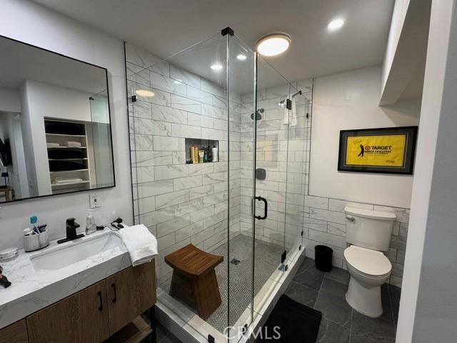 bathroom featuring toilet, a shower with shower door, tile patterned flooring, tile walls, and vanity