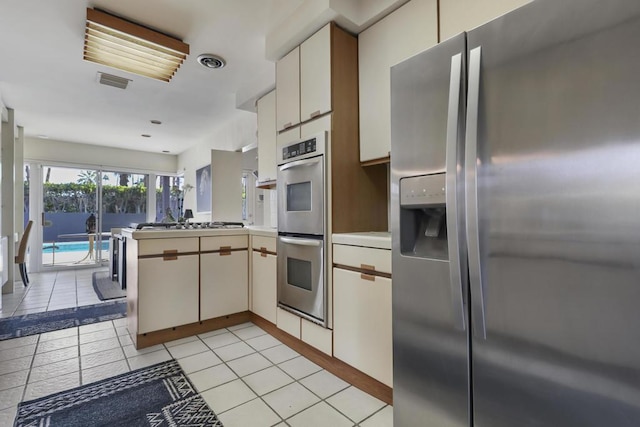 kitchen with light tile patterned floors, appliances with stainless steel finishes, kitchen peninsula, and white cabinets