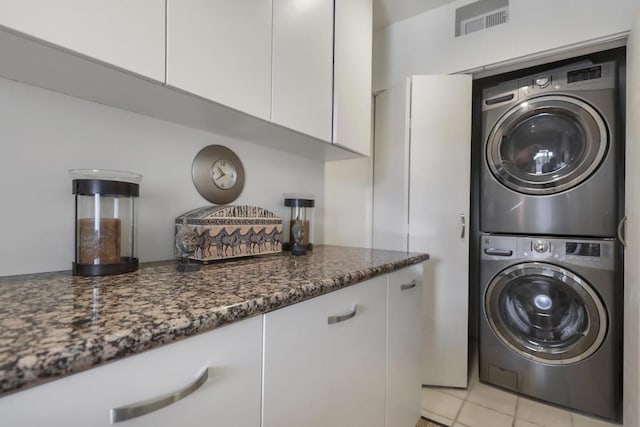 laundry area with stacked washer / drying machine and light tile patterned floors