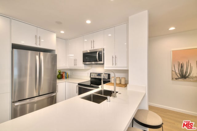 kitchen featuring a breakfast bar, sink, light wood-type flooring, appliances with stainless steel finishes, and white cabinets