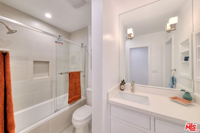 full bathroom with bath / shower combo with glass door, toilet, and vanity