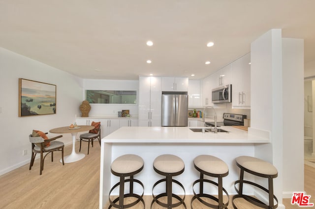 kitchen featuring white cabinetry, stainless steel appliances, sink, kitchen peninsula, and light wood-type flooring